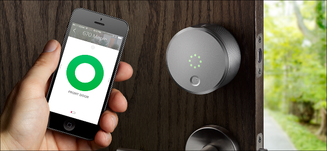 A man's hand holding an iPhone showing the August Smart Lock app and opening a door with an August Smart lock on it.